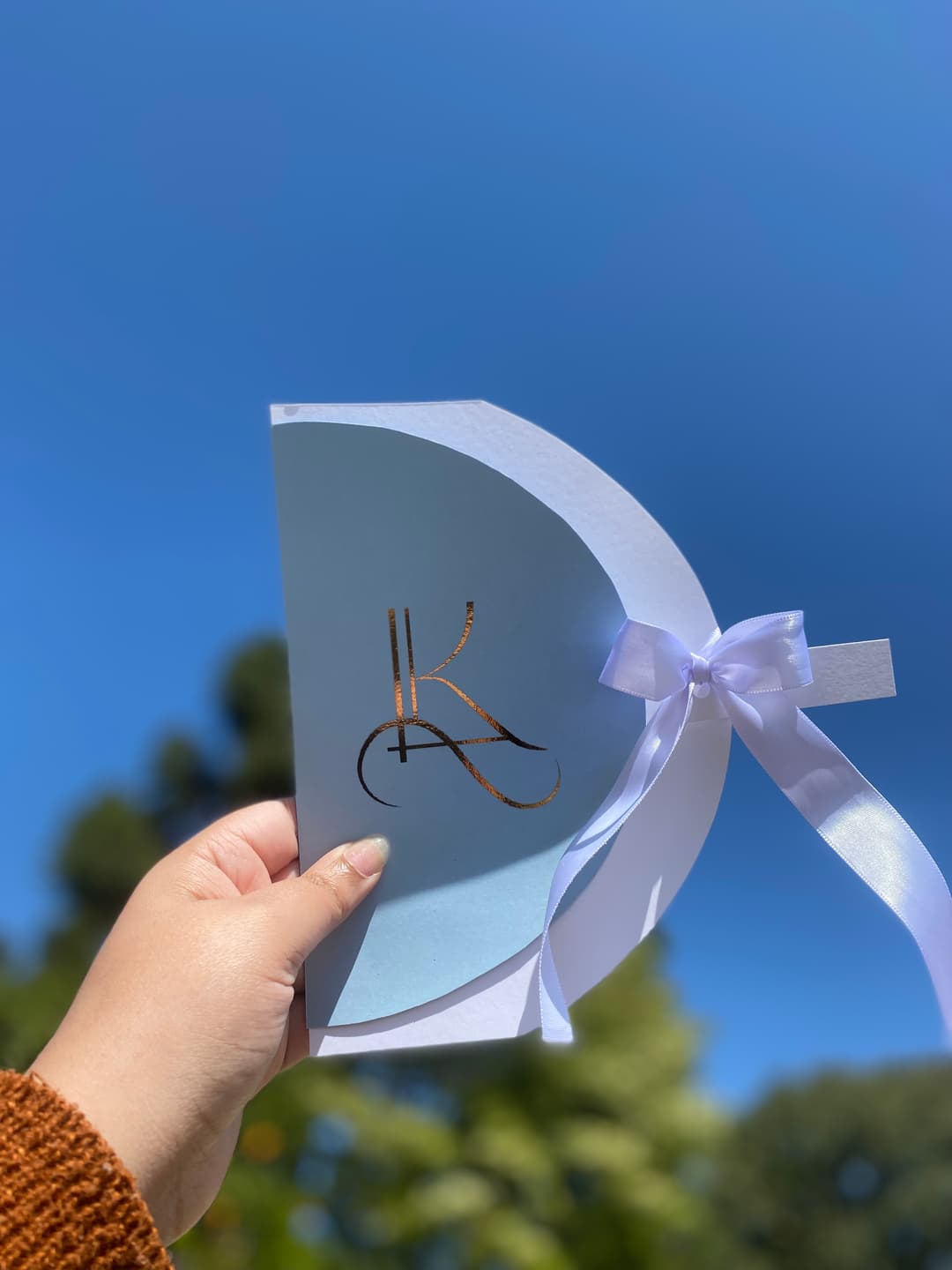 Convite de casamento azul em formato leque segurado contra o céu